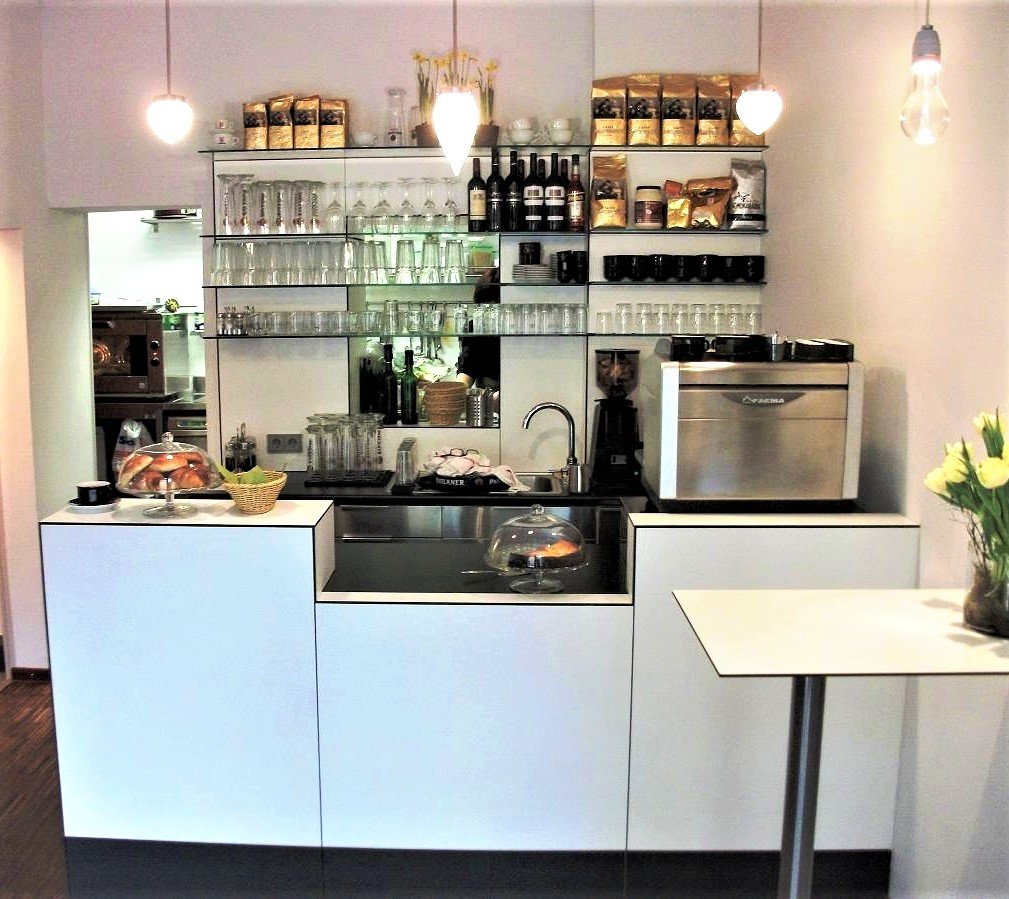 Weiße Theke mit Kaffeemaschine und einer Regalwand mit Gläsern und Kaffeepackungen