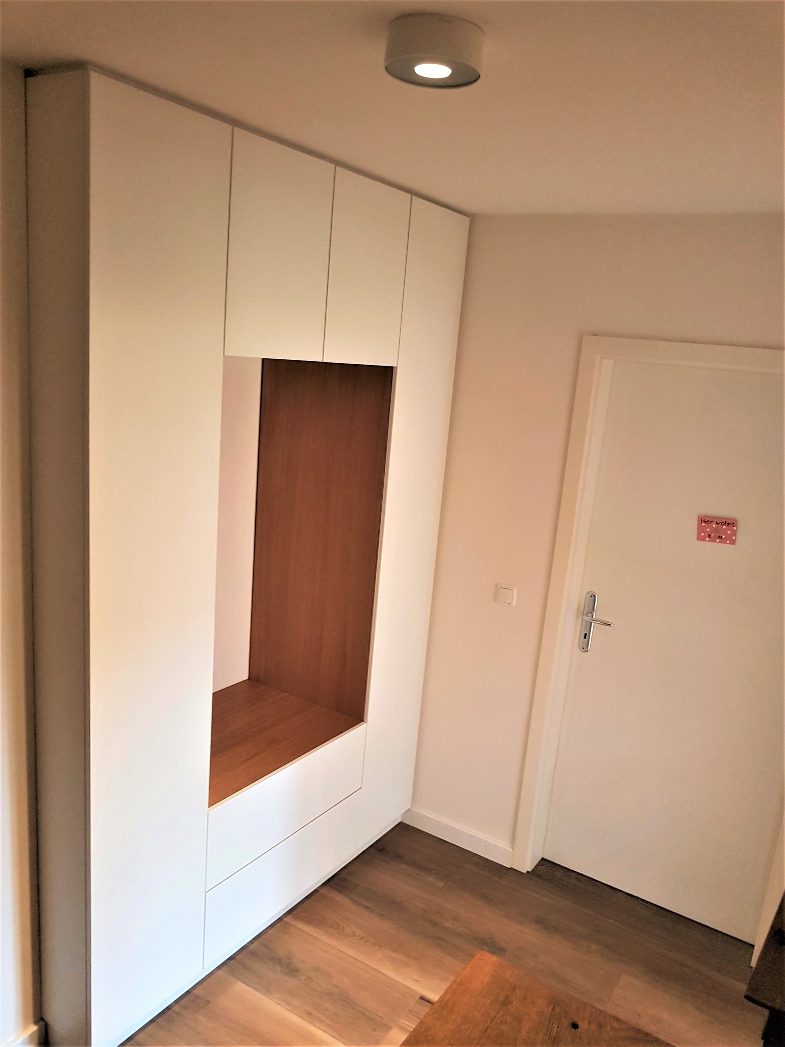 Weißer Einbauschrank in einem Flur mit einer Nische mit Holzeinsatz und einem Spot darüber